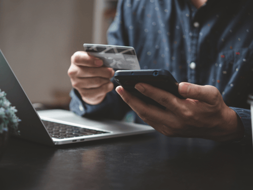 Un homme tient une carte de crédit dans sa main droite et son téléphone mobile dans la main gauche