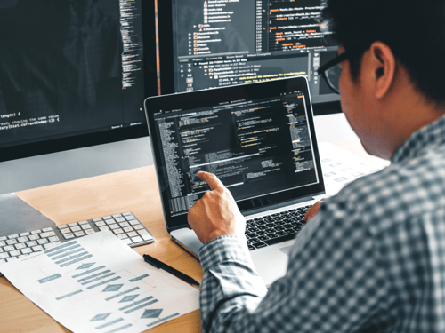 Developer working on a laptop, coding an application with multiple screens showing code and diagrams in the background